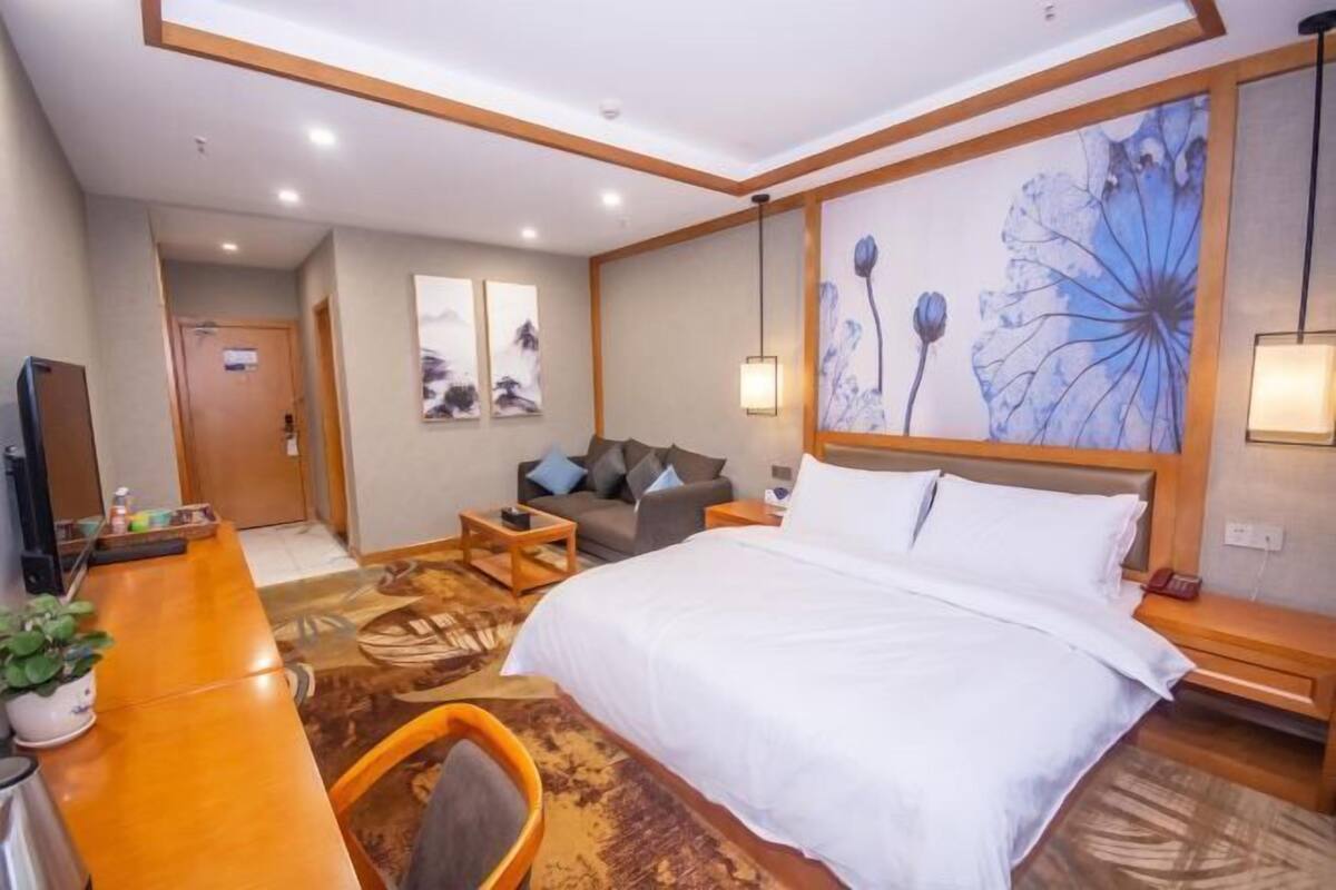A hotel room with a large bed, a sofa, a desk with a chair, and a wall with floral artwork.