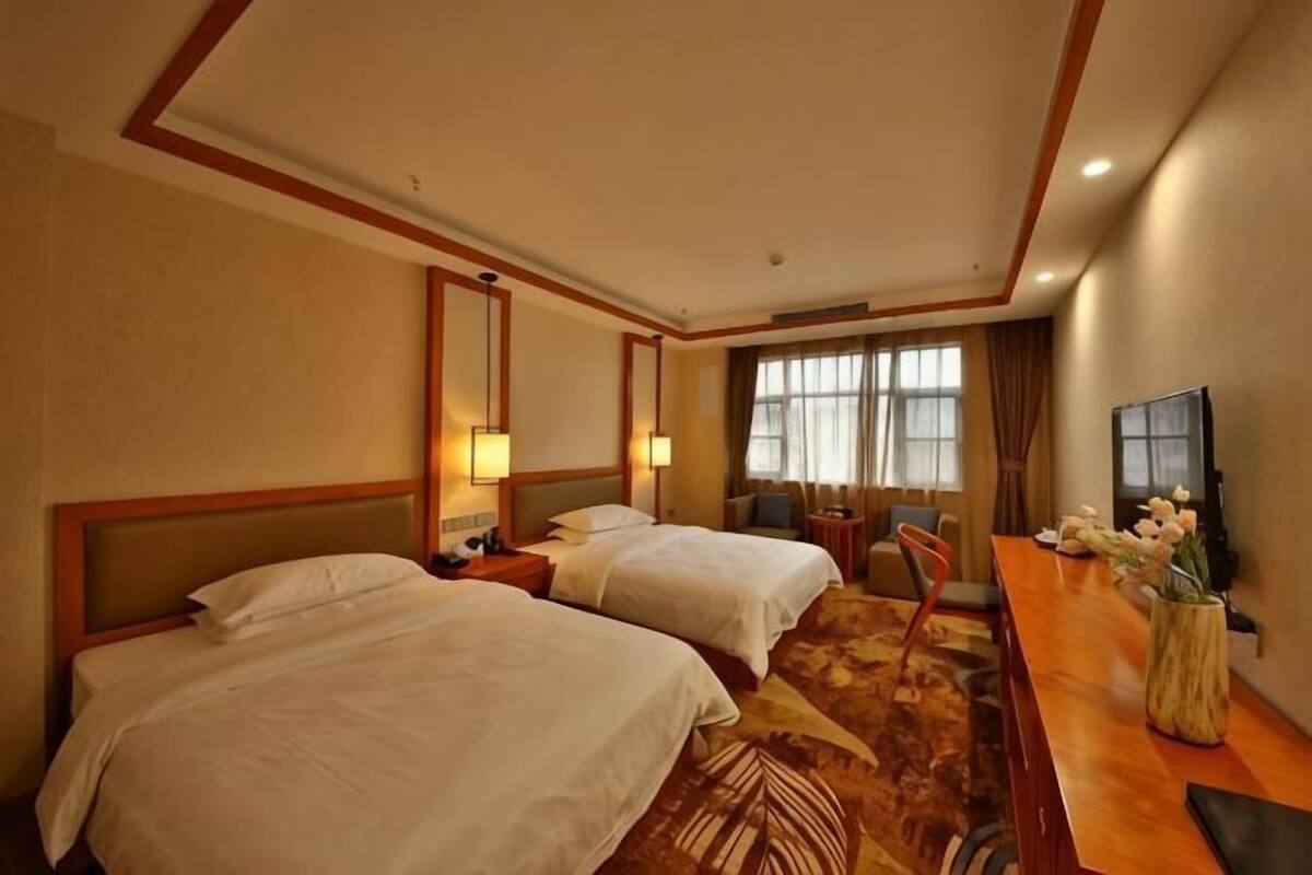 A hotel room with two beds, a desk, a chair, a TV, and a window with curtains.