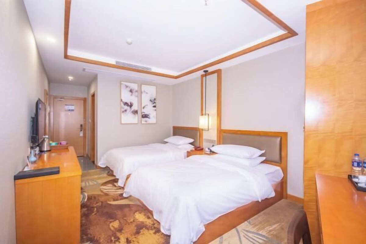 A hotel room with two beds, a desk, a mirror, and artwork on the wall.