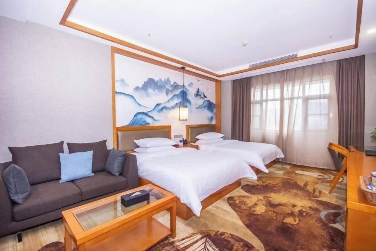 A hotel room with a bed, a sofa, a coffee table, and a painting on the wall.