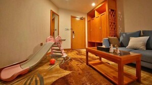 A room with a sofa, a wooden cabinet, a small table, and a children's play area. - Mingdelou Hotel (Yichang)