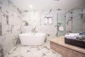 A modern bathroom with a freestanding bathtub, marble-tiled walls, and a glass shower enclosure. - Mingdelou Hotel (Yichang)