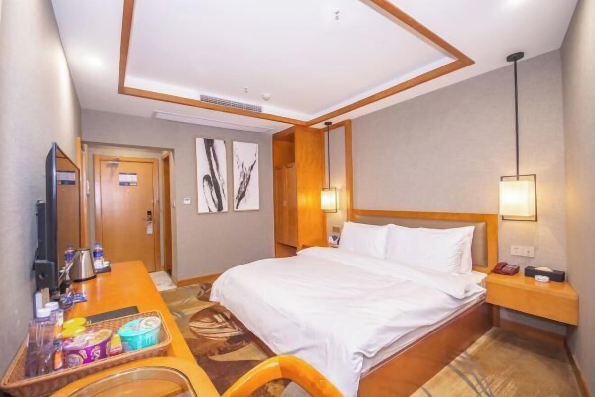 A hotel room with a bed, a desk with a chair, a television, and a tray with snacks.