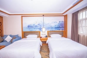 Habitación de hotel con dos camas, un sofá, un cuadro de un paisaje y una mesita de noche con lámpara.