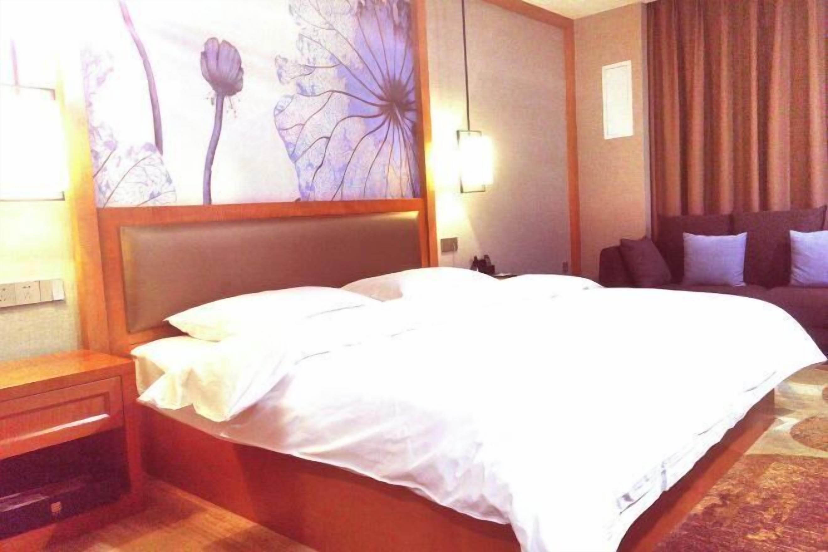 A hotel room with a large bed, a nightstand, a wall-mounted lamp, and a view of the outdoors.