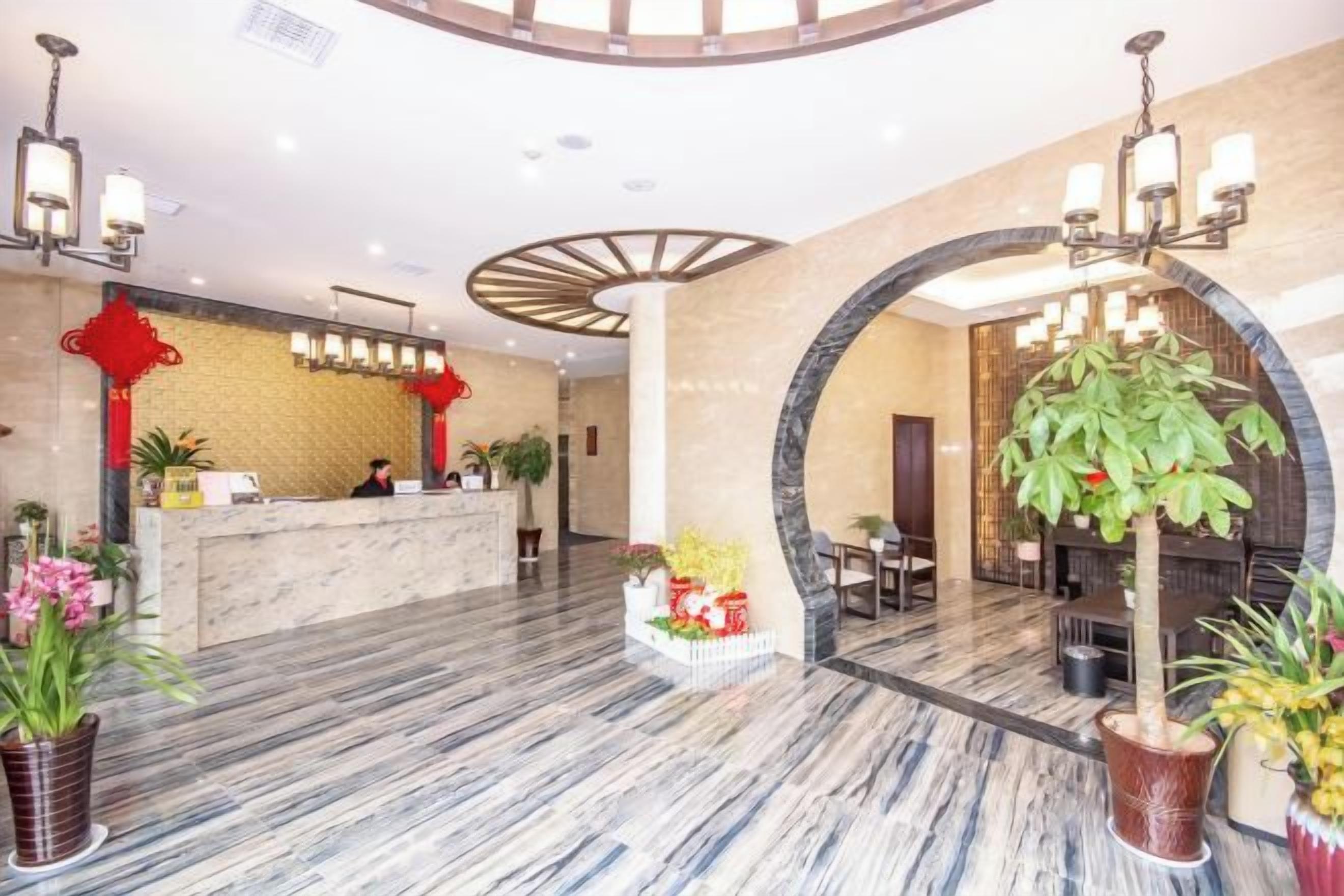 Un hall de hotel con mostrador de recepción, zona de estar y plantas decorativas.