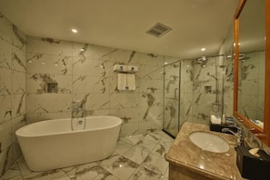 Un baño con una bañera independiente, un lavabo con encimera de mármol y ducha con mampara de vidrio.