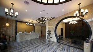 A hotel lobby with a reception desk, seating area, and a large circular wall feature. - Mingdelou Hotel (Yichang)