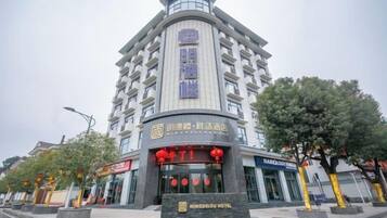 Un hotel de varios pisos con una entrada destacada, señalización y un área ajardinada con árboles.