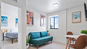 Ein modernes Wohnzimmer mit einem türkisfarbenen Sofa, einem Esstisch mit braunen Stühlen und Kunstwerken an den Wänden.
