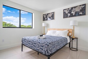 Ein modernes Schlafzimmer mit einem großen Bett, zwei Nachttischlampen, einer Weltkarte an der Wand und einem Fenster mit Blick auf Bäume.
