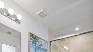 Ein modernes Badezimmer mit einem weißen Waschtisch, einer Toilette, einer Glasdusche und einem gerahmten Bild an der Wand.