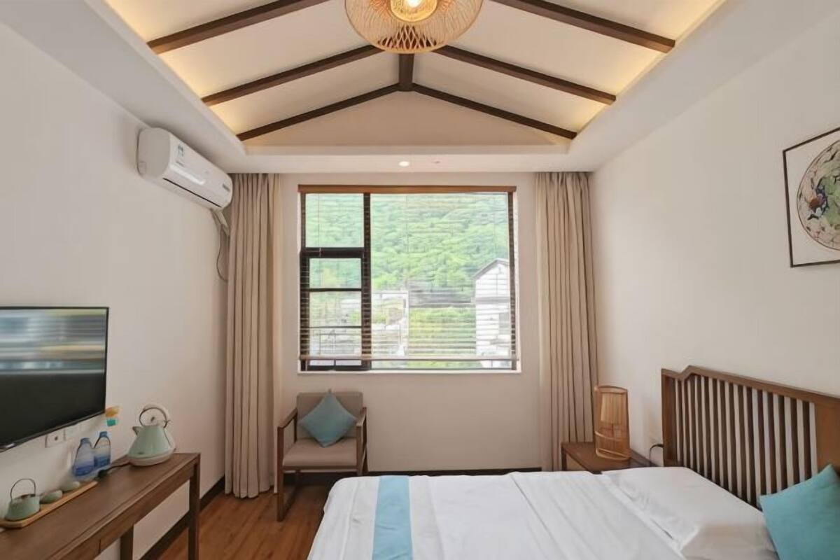 A bedroom with a bed, a television, a window with curtains, a chair, and a bedside table.