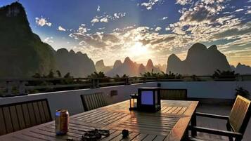 A wooden table with chairs, a laptop, and a can on a balcony overlooking a mountainous landscape.