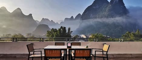 A terrace with a table and chairs, overlooking a mountainous landscape.