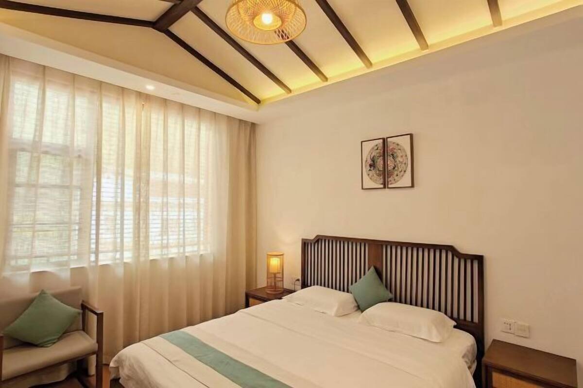 A hotel room with a bed, a nightstand, a lamp, a chair, and a window with curtains.