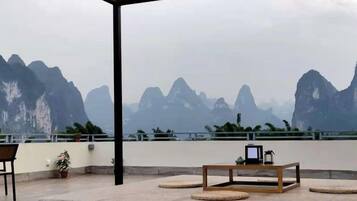 An outdoor seating area with a table and chairs, overlooking a body of water and mountains.