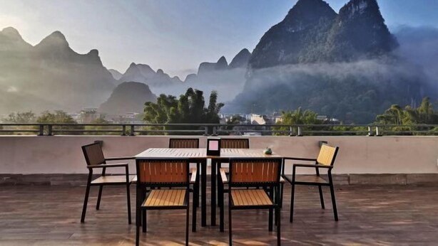 Una terraza con mesa y sillas, con vistas a un paisaje montañoso cubierto de niebla y un cielo despejado.