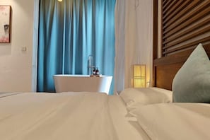 Hotellihuone, jossa on sänky, valkoinen yöpöytä, sininen verho ja puinen pääty.