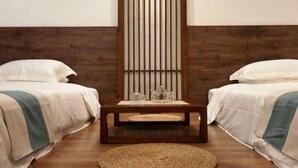 Una habitación con dos camas, piso de madera, alfombra tejida y un panel de madera vertical.