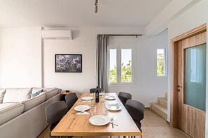 Zona de menjador amb taula de fusta per a quatre, un sofà, un quadre amb marc a la paret i una finestra amb cortines.