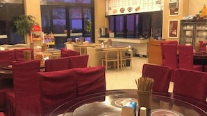 Een restaurant met ronde tafels, rode bekleden stoelen en een menubord aan de muur.
