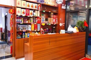 A reception desk with a wooden finish, shelves stocked with various products, and a glass display case. - Yanzhu Hotel (Anhua)