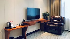 Een hotelkamer met een flatscreen televisie, een houten bureau, een leren bank en een potplant.