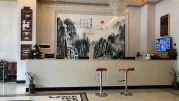 A reception area with a large wall painting, a television, and two bar stools.