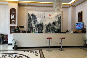 A reception area with a large wall painting, a television, and two bar stools. - Yanzhu Hotel (Anhua)