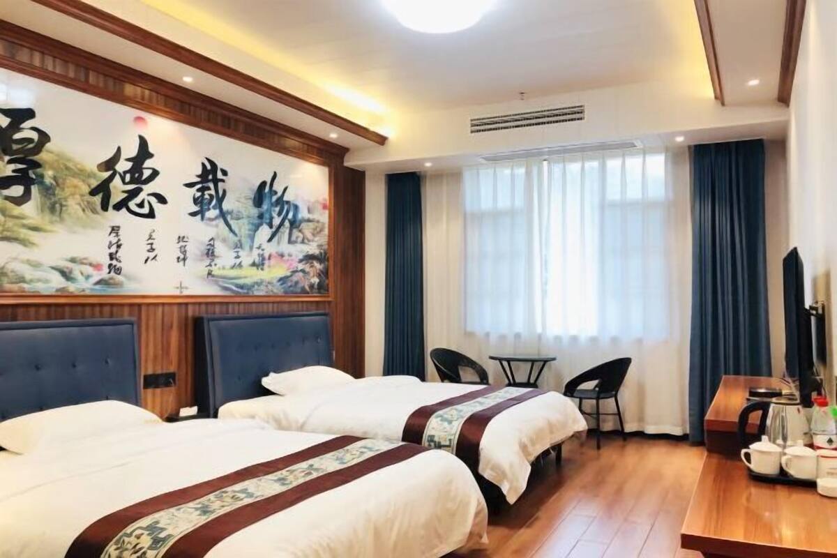 Quarto de hotel com duas camas, uma escrivaninha de madeira, uma cadeira e um quadro grande na parede.