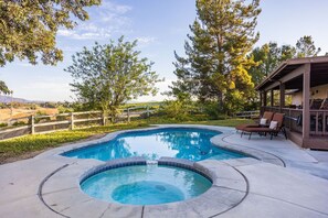 Zwembad met een jacuzzi, omringd door een houten terras en ligstoelen, met bomen en een verre horizon.