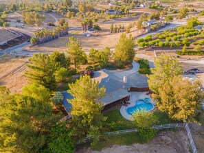 A residential property with a large swimming pool, a fenced yard, and a house with a sloped roof.