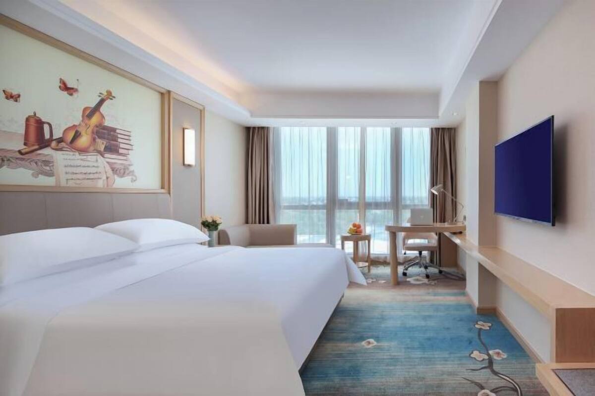 A hotel room with a large bed, a desk, a chair, a flat-screen TV, and a window with curtains.