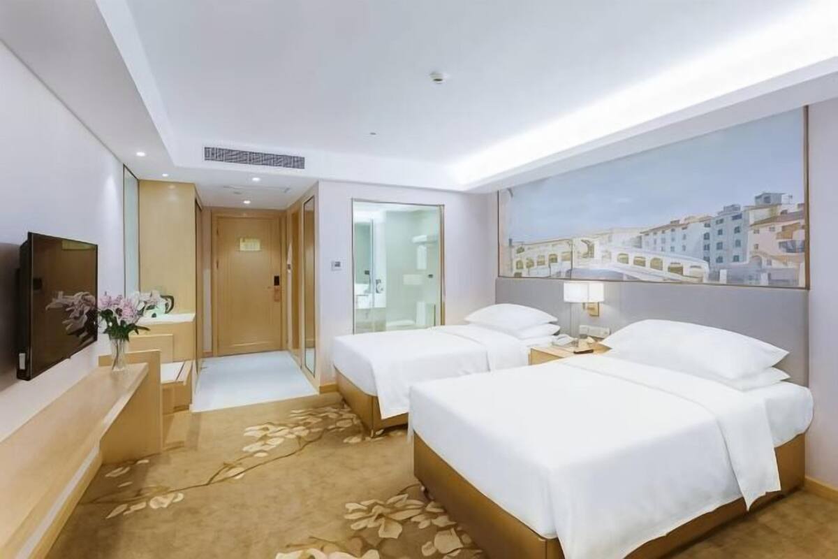 A hotel room with two beds, a TV, a desk with a lamp, and a painting on the wall.