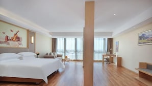 A hotel room with a large bed, a desk, and a view of the outdoors. - Vienna International Hotel (Qidong)