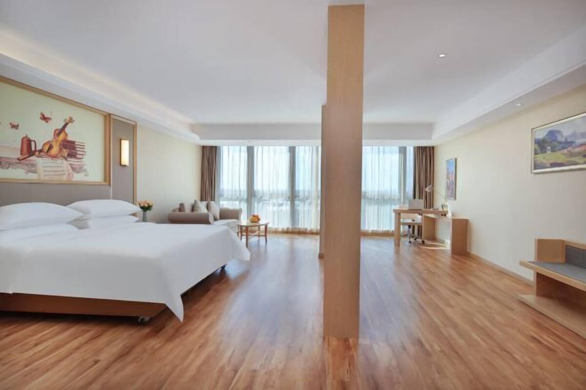 A hotel room with a large bed, a desk, and a view of the outdoors.