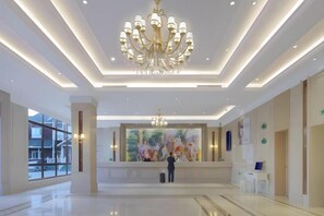 Eine geräumige Lobby mit einem großen Chandelier, einem Empfangsschalter und einem großen Fenster mit Blick nach außen.