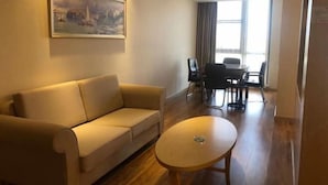 A living room with a sofa, a coffee table, a painting on the wall, and a dining area with chairs and a table. - Vienna International Hotel (Qidong)