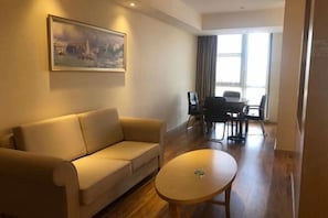 A living room with a sofa, a coffee table, a painting on the wall, and a dining area with chairs and a table. - Vienna International Hotel (Qidong)