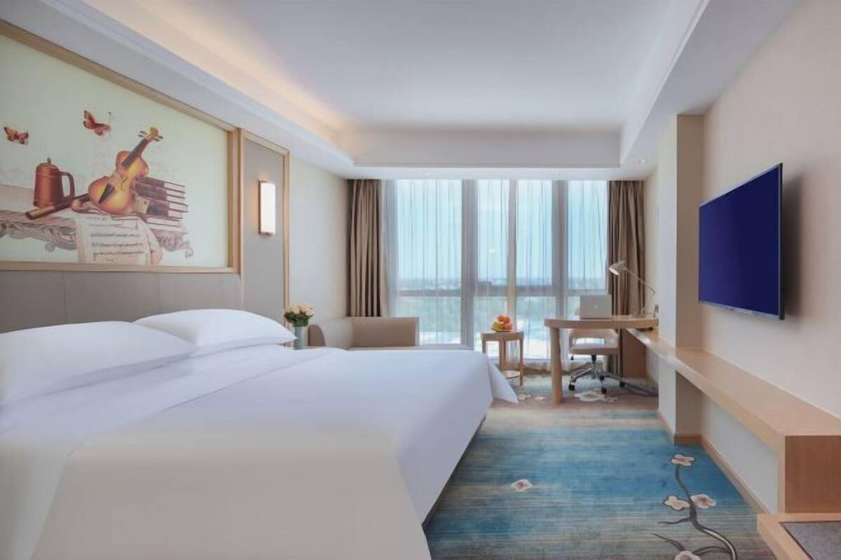 A hotel room with a large bed, a desk, a chair, a TV, and a window with curtains.
