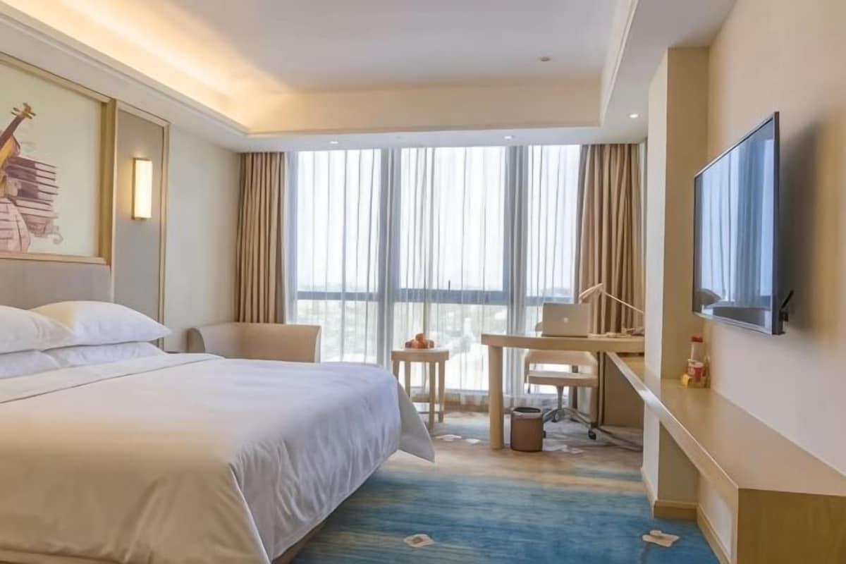A hotel room with a large bed, a desk, a chair, a television, and a window with curtains.