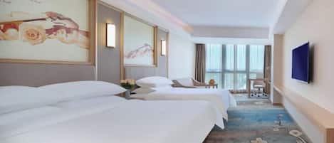 Habitación de hotel con dos camas, un ventanal grande, un televisor de pantalla plana y una alfombra estampada con motivos florales.