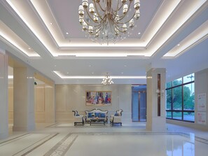 A spacious lobby with a chandelier, a painting, and a seating area. - Vienna International Hotel (Qidong)