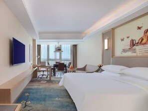 Een hotelkamer met een groot bed, een bureau met stoel, een aan de muur bevestigde televisie en een raam met gordijnen.