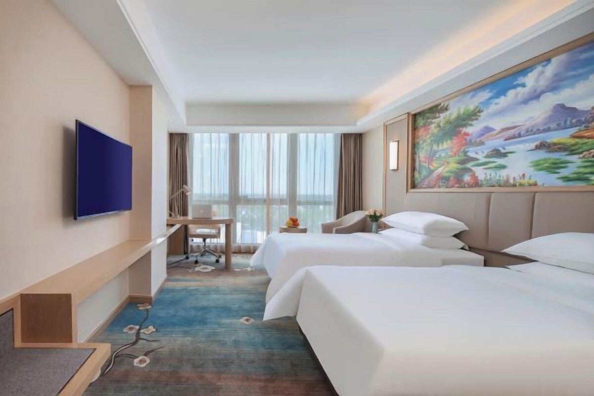 Een hotelkamer met twee bedden, een bureau, een televisie en een groot raam.