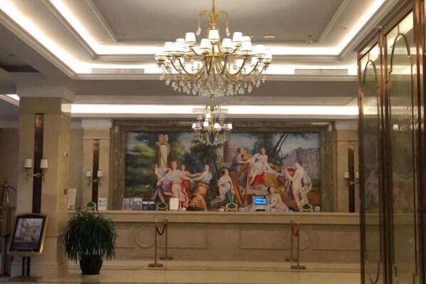 A lobby with a large mural, a chandelier, and a potted plant. - Vienna International Hotel (Qidong)