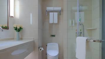 A modern bathroom with a glass shower enclosure, a toilet, and a sink with a vase of flowers.