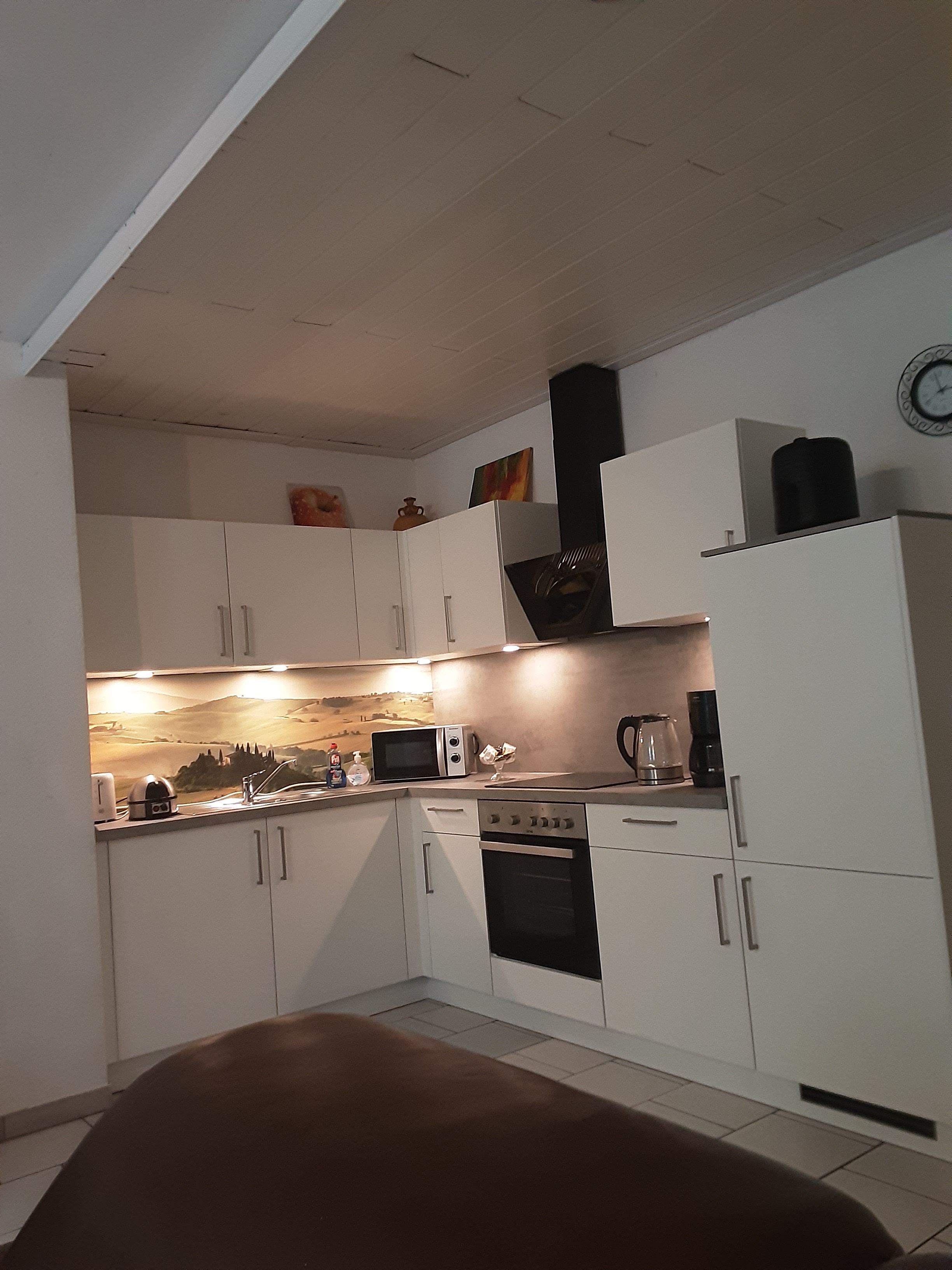 A kitchen with white cabinets, a microwave, a coffee maker, and a clock on the wall.