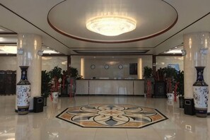 Un vestíbulo de hotel con mostrador de recepción, jarrones grandes y un diseño decorativo en el suelo.